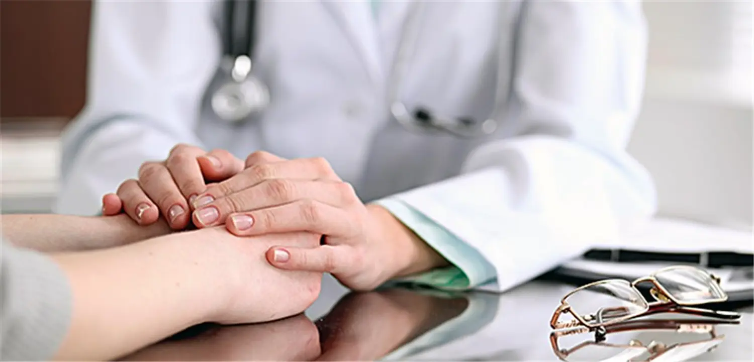 Frauenarztpraxis-Faur - Gynäkologie und Geburtshilfe - Eine Ärztin im weißen Kittel mit einem Stethoskop um den Hals hält während einer Konsultation die Hände eines Patienten.